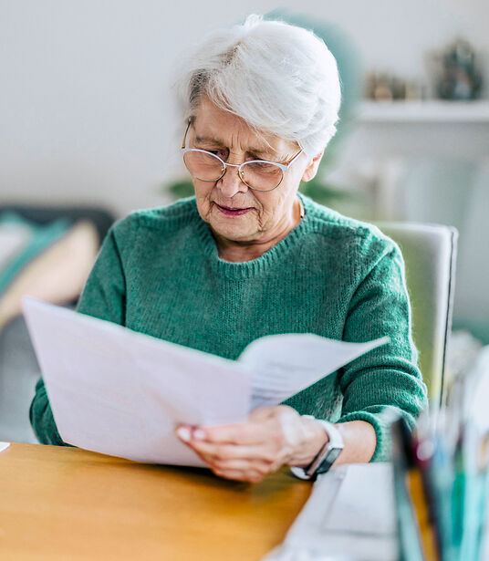 Seniorin liest Unterlagen Ältere Frau liest am Tisch ein Schreiben
